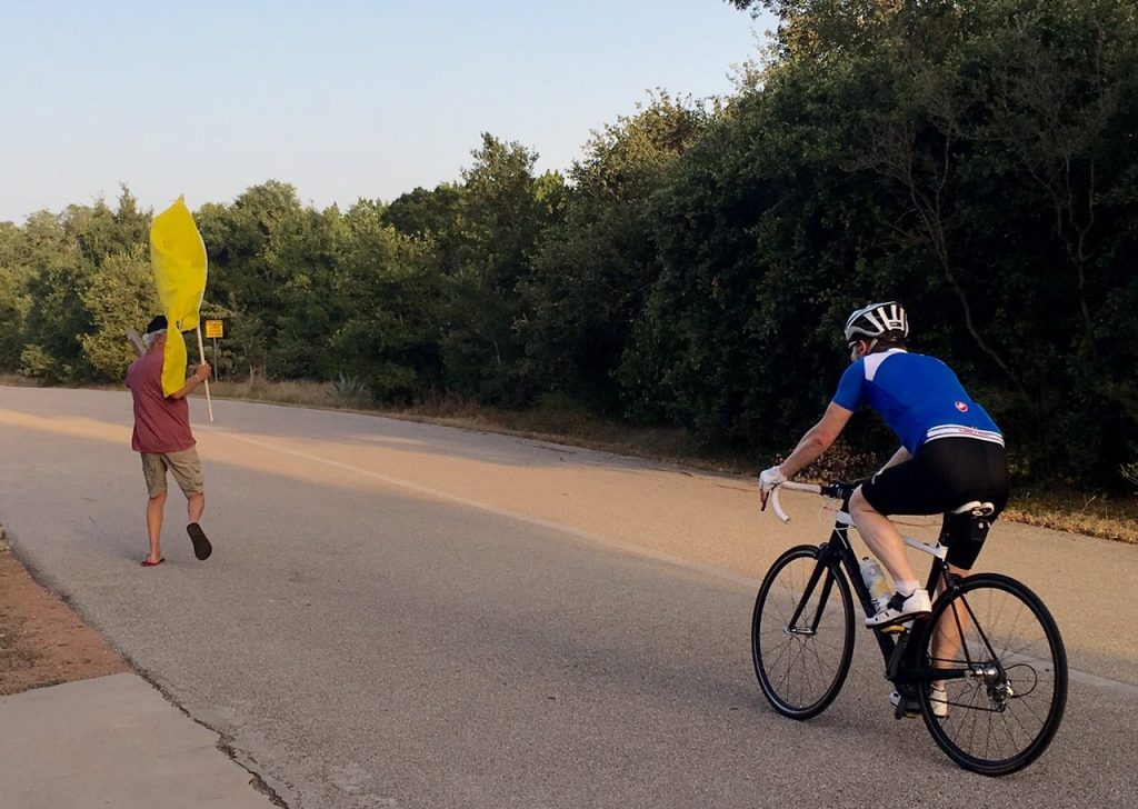 Jayme Edwards riding his bike at The Veloway in Austin, Texas while his father-in-law eggs him on with a "Don't Tread on Me" flag.